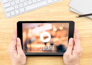 Hand holding tablet with Video sharing on screen on table