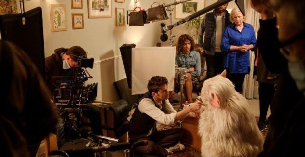 Film crew captures a staged indoor scene with a large dog and actors