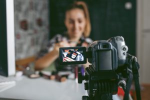Smiling Teenage girl making her video blog about makeup. She is using home video camera to record video blogs and publish online. Selective focus to camera screen. She is blogger and vlogger.